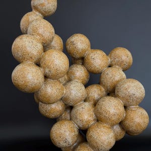 May include: A sculptural object composed of numerous interconnected spheres of varying sizes. The spheres feature a textured, speckled tan and brown finish, resembling natural stone or granite, arranged in an organic, clustered, and asymmetrical formation.