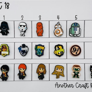 May include: A collection of character-themed shoe charms, including Star Wars and Harry Potter designs. The charms are arranged in rows and columns on a white background. The text "lot 18" and "Another Craft Room" are visible.