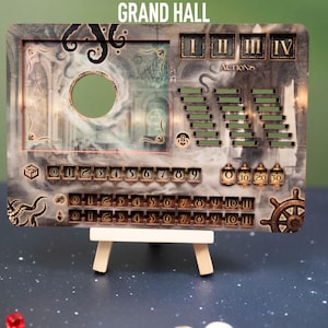 May include: A decorative game board with the text "GRAND HALL". The board features a circular cutout, action trackers, and number indicators. It is supported by a small wooden easel. The color scheme includes shades of gray, brown, and gold.