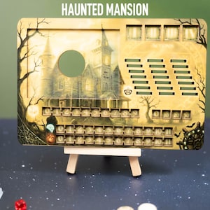 May include: A Haunted Mansion themed game board with a spooky haunted house illustration. The board has a series of numbered slots and cutouts. The text "HAUNTED MANSION" is at the top. The board is propped up on a small wooden easel.