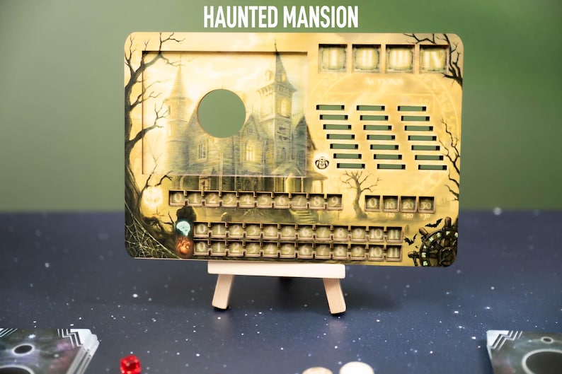 May include: A Haunted Mansion themed game board with a spooky haunted house illustration. The board has a series of numbered slots and cutouts. The text "HAUNTED MANSION" is at the top. The board is propped up on a small wooden easel.