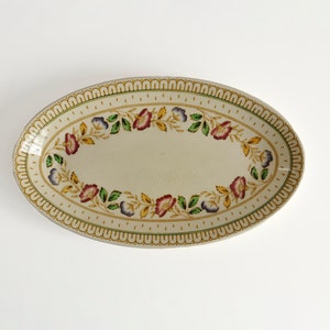 May include: Oval serving platter with a floral design. The off-white ceramic platter features a border of repeating arches and a central floral pattern with red, purple, and yellow flowers and green leaves.