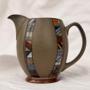 Peut inclure: Pichet en céramique marron avec un motif mosaïque décoratif de rectangles dans les tons de bleu, orange et marron. Le pichet a une anse incurvée et un bec verseur. La base est de couleur marron foncé.