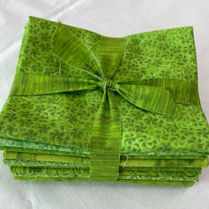 May include: A stack of green fabric squares tied with a green ribbon. The fabric has a variety of patterns, including swirls, dots, and leaves.