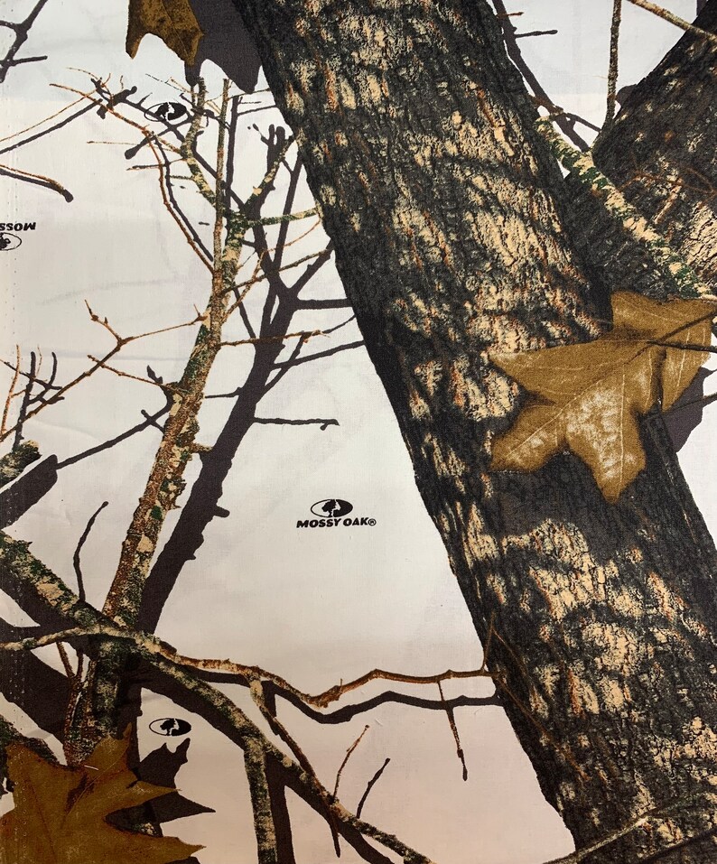 May include: White fabric with a camouflage pattern featuring brown, black, and green branches and leaves. The fabric has the words "Mossy Oak" printed in black.