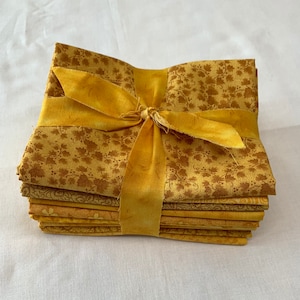 May include: A stack of eight yellow fabric squares with a brown floral pattern, tied together with a yellow ribbon.