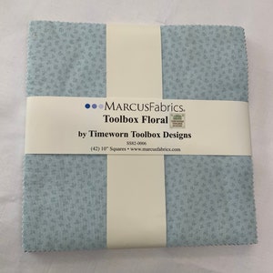 May include: A pack of 42, 10-inch fabric squares featuring a light blue background with a small white floral pattern. The pack is labeled "Toolbox Floral" by Timeworn Toolbox Designs.  The label also includes the text "MARCUSFabrics" and "SS82-0006".