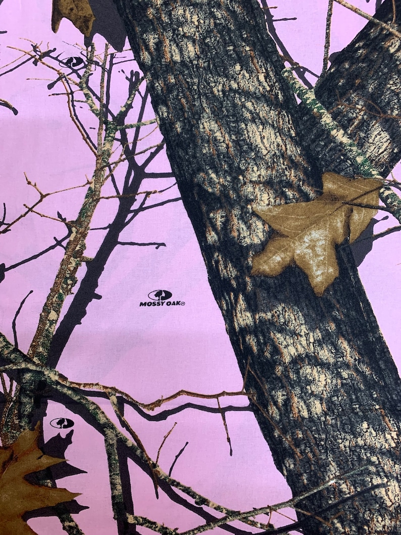 May include: Pink camouflage fabric with a black and brown tree pattern. The fabric has the Mossy Oak logo in the center.