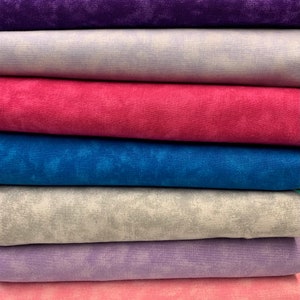 Pode incluir: Uma pilha de seis quadrados de tecido em várias tonalidades de roxo, rosa, azul e cinza. O tecido tem um padrão sutilmente salpicado.