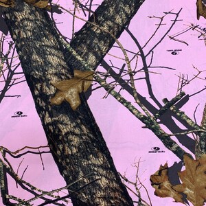 May include: Pink camouflage fabric with a tree trunk pattern and the Mossy Oak logo repeated throughout.