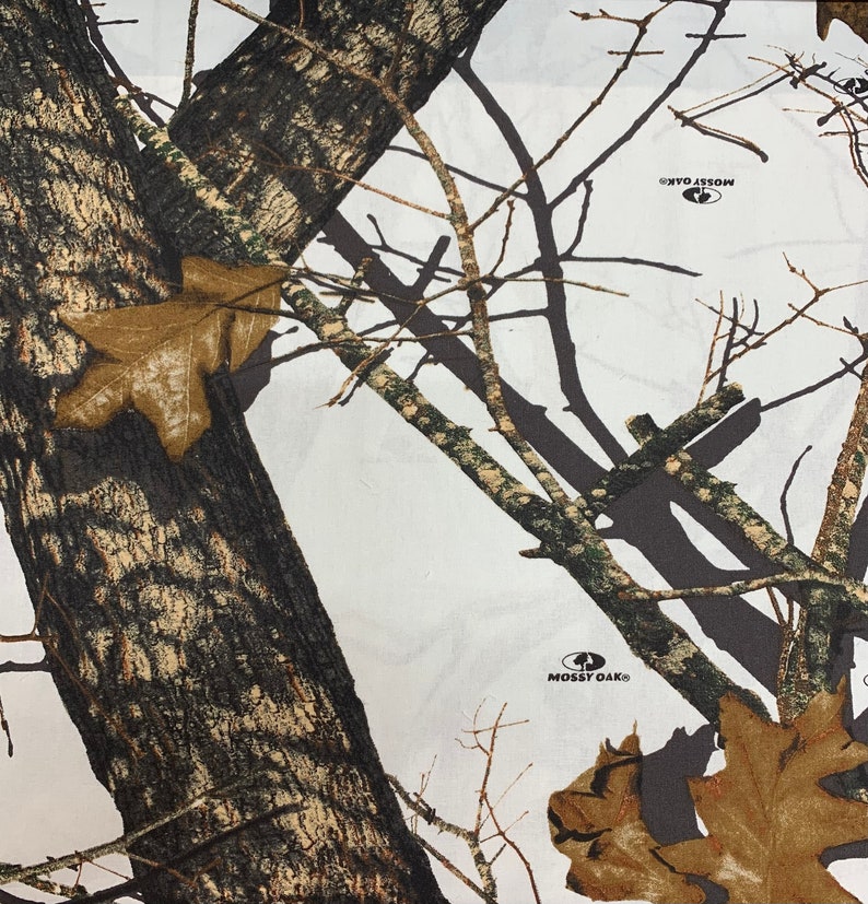 May include: White camouflage fabric with brown and green tree branches and leaves. The fabric has the Mossy Oak logo printed on it.