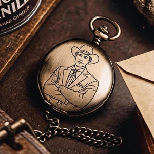May include: A round, antique-finish bronze pocket watch featuring an engraved illustration of a person wearing a cowboy hat and a suit with a bolo tie. The watch includes a matching metal chain and a circular top loop for attachment.
