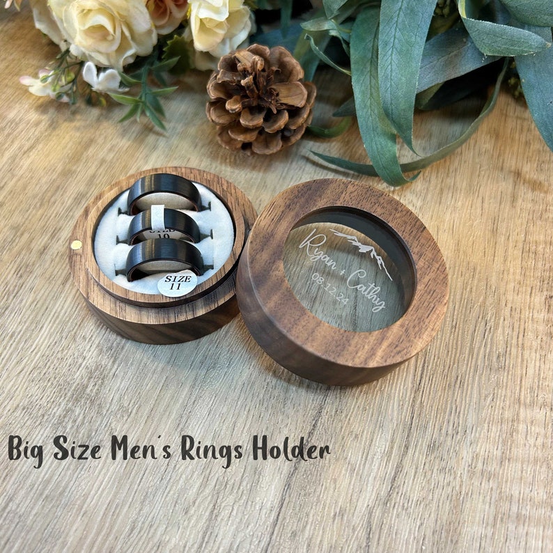 K&ouml;nnte beinhalten: Eine Holzkiste f&uuml;r Ringe mit einem durchsichtigen Deckel. Der Deckel ist mit dem Text "Ryan + Cathy 08.12.24" graviert. Die Box hat ein Samt-Innenfutter mit Schlitzen f&uuml;r Ringe. Die Box ist mit "Big Size Men's Rings Holder" beschriftet.