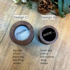 K&ouml;nnte beinhalten: Zwei Holzringehalter, einer gro&szlig; und einer klein. Der gro&szlig;e Halter hat einen Durchmesser von 6,7 cm und drei F&auml;cher. Der kleine Halter hat einen Durchmesser von 5 cm und zwei F&auml;cher. Beide Halter sind aus dunklem Holz und haben eine glatte Oberfl&auml;che.