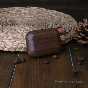 May include: A dark brown wooden case for AirPods, made from North American walnut wood. The case is sitting on a wooden surface with coffee beans scattered around it.