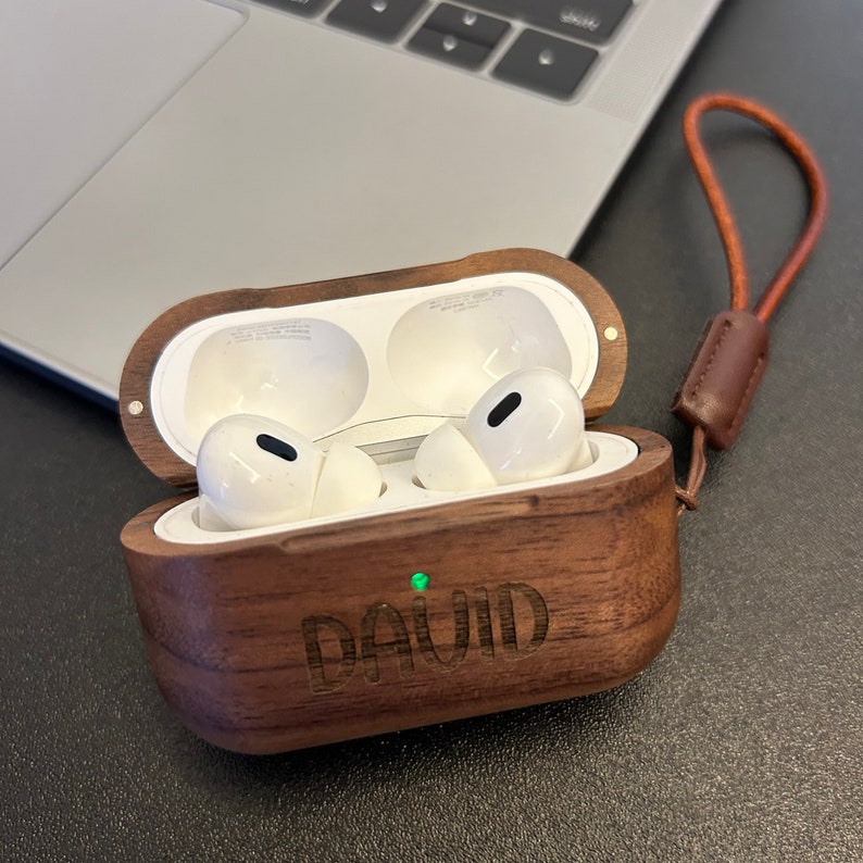 May include: A wooden case for wireless earbuds with a personalized inscription that reads "DAVID". The case is brown with a light brown leather strap.