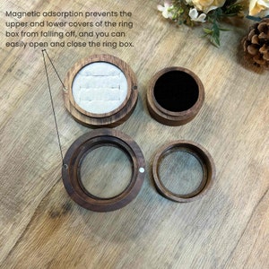 K&ouml;nnte beinhalten: Eine Holzschachtel f&uuml;r Ringe mit magnetischem Verschluss. Die Schachtel ist aus dunklem Holz und hat ein Samtfutter. Die Schachtel ist ge&ouml;ffnet und der Deckel liegt daneben. Die Schachtel ist f&uuml;r einen Ring gedacht.