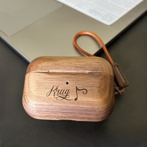 May include: A wooden case for wireless earbuds with a leather strap. The case is engraved with the word "Krug" and a musical note.