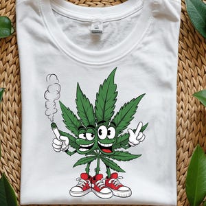 Peut inclure: T-shirt blanc avec un personnage de feuille de cannabis de dessin animé. La feuille verte a un visage souriant, un joint allumé et fait le signe de la paix. Il porte des baskets rouges. Le motif est centré sur le t-shirt.