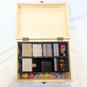 May include: A wooden box with a hinged lid, containing multiple compartments. The compartments are filled with small plastic pieces and cards. The box is open and the lid is propped up.