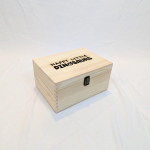 May include: A wooden box with a hinged lid and a latch. The box is made of light wood and has the words "Happy Little Dinosaurs" engraved on the top.
