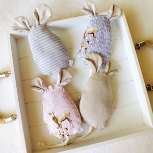 Könnte beinhalten: Vier handgefertigte Plüschmausspielzeuge in einer weißen Schale mit Seilgriffen. Die Mäuse sind aus verschiedenen Stoffen mit verschiedenen Mustern gefertigt, darunter Streifen, Hirschdrucke und ein einfarbiger beigefarbener Stoff.