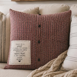 May include: A decorative pillow with a red and black plaid pattern, resembling a shirt. The pillow has three dark buttons and a patch with the text "THIS IS A shirt I USED TO WEAR whenever you HOLD IT know that I AM THERE LOVE, BUBBA".