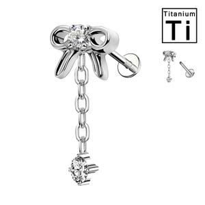 Op de afbeelding: Een zilverkleurige oorbel in de vorm van een strik met een bungelende ketting en een sprankelende edelsteen aan het einde. De oorbel heeft een platte achterkant en een pin voor piercing. De afbeelding bevat ook een kleine afbeelding met de tekst "Titanium Ti".