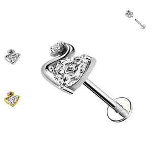 Puede incluir: Joyería corporal de plata con una piedra preciosa transparente en forma de pera y una piedra preciosa transparente más pequeña en un engaste curvo. La joyería está diseñada para un piercing de cartílago.