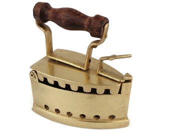 May include: A vintage brass iron with a wooden handle. The iron has a rounded base with a series of holes and a hinged top.