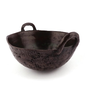 May include: A dark brown ceramic bowl with two handles. The bowl has a rough, textured surface.