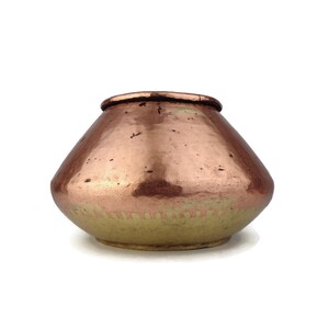 Op de afbeelding: Een kleine koperen pot met een ronde bodem en een licht uitlopende rand. De pot heeft een gehamerde afwerking en een warme, gouden tint.