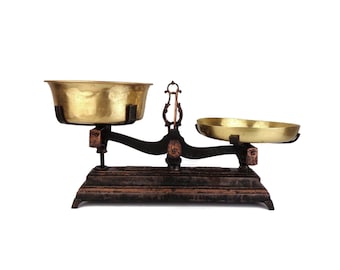 May include: A vintage brass and black balance scale with two round bowls. The scale is made of metal and has a rustic, antique look.
