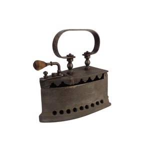 Puede incluir: Una plancha de hierro fundido antigua con un mango de madera y un mango de metal en la parte superior. La plancha tiene una serie de agujeros en la parte inferior y un diseño decorativo en el lateral.