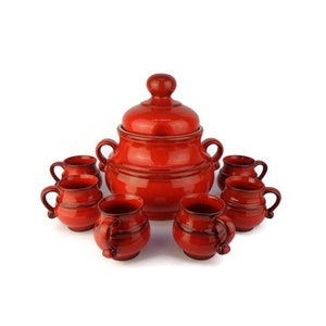 Può includere: Un set di tazze in ceramica rossa e una grande brocca in ceramica rossa con coperchio. Le tazze e la brocca hanno un aspetto rustico e fatto a mano.