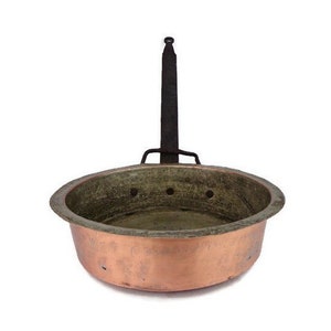 May include: A copper pot with a black iron handle. The pot has a round shape and a slightly flared rim. There are several small holes in the bottom of the pot.