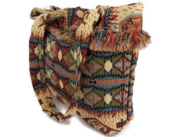 Puede incluir: Un bolso tote grande y colorido con un patrón geométrico en tonos azules, rojos, verdes y beige. El bolso tiene un borde con flecos y una correa larga.