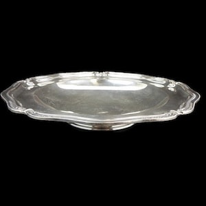 May include: A silver serving dish with a scalloped edge and a raised center. The dish is made of polished metal and has a shiny finish.