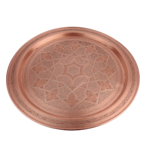 May include: A round copper serving tray with an intricate engraved design. The tray has a raised rim and a polished finish.
