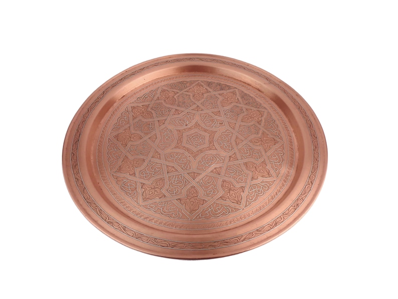 May include: A round copper serving tray with an intricate engraved design. The tray has a raised rim and a polished finish.
