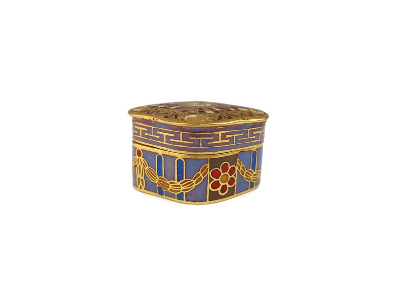 May include: A small, square, decorative box with a blue, purple, and gold enamel design. The box has a geometric pattern and floral accents.