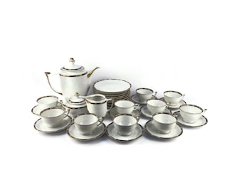 May include: A white porcelain tea set with gold trim. The set includes a teapot, creamer, sugar bowl, and 12 teacups and saucers.