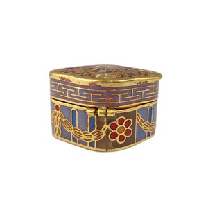 May include: A small, square, decorative box with a hinged lid. The box is made of metal and is decorated with a colorful enamel design. The design features a floral pattern, geometric shapes, and gold accents.