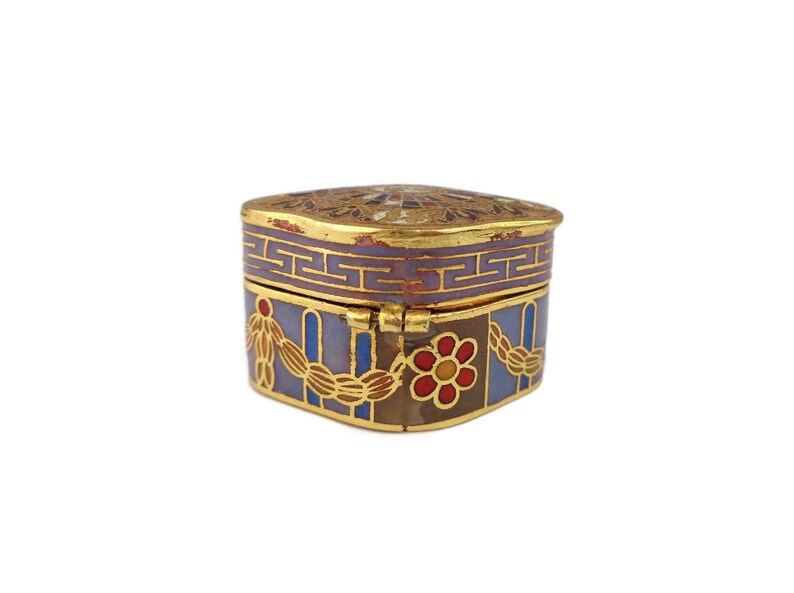 May include: A small, square, decorative box with a hinged lid. The box is made of metal and is decorated with a colorful enamel design. The design features a floral pattern, geometric shapes, and gold accents.