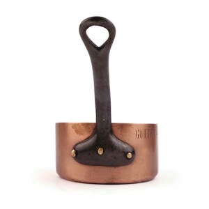 Peut inclure: Une petite casserole en cuivre avec une poignée en métal foncé. La poignée est fixée avec deux rivets. Le mot "GUIT" est estampillé sur le côté. Idéale pour la cuisine, elle mesure environ 10 cm de diamètre.