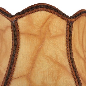 May include: A tan lampshade with a brown scalloped trim. The lampshade has a textured surface and is made of a fabric material.