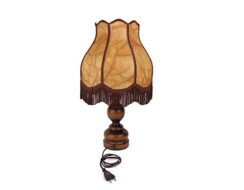 May include: A wooden table lamp with a brown and beige patterned lampshade. The lampshade has a fringe trim and the base is a dark wood.