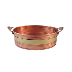 May include: An oval copper-coloured metal tub with two ornate handles. A wide, gold-coloured band encircles the middle. The tub has a ribbed texture. The background is white.