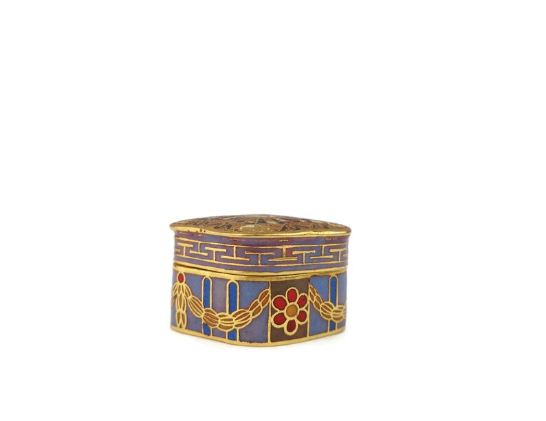 May include: A small, square, decorative box with a gold lid and blue, purple, red, and gold enamel designs. The box has a geometric pattern on the top and a floral design on the sides.
