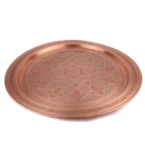 May include: A round copper serving tray with an intricate engraved design. The tray has a raised rim and a polished finish.